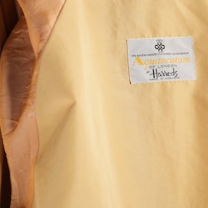 May include: A beige jacket with a brown satin lining. The jacket has a label that reads "Aquascutum of London at Harrods Made in England".