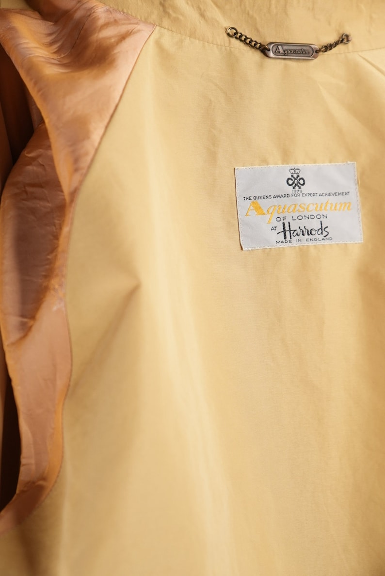 May include: A beige jacket with a brown satin lining. The jacket has a label that reads "Aquascutum of London at Harrods Made in England".