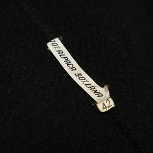 May include: A white label with black text that reads "70% Alpaca 30% Lana" and the number "42" on a black fabric background.