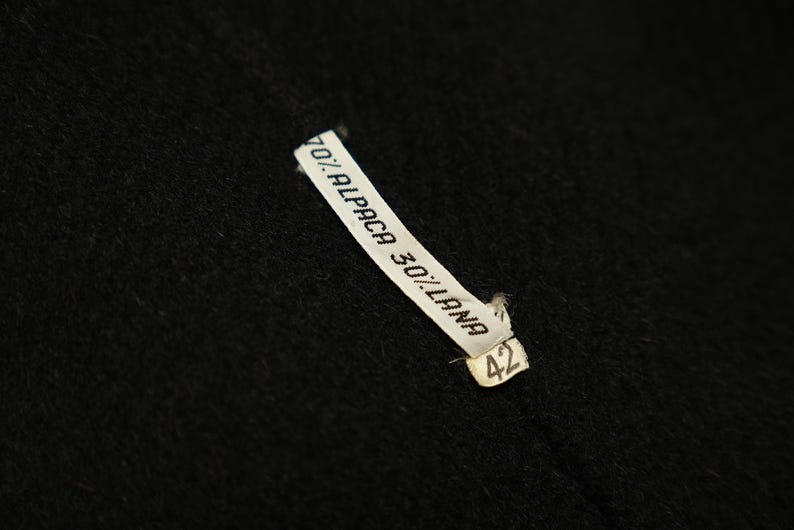 May include: A white label with black text that reads "70% Alpaca 30% Lana" and the number "42" on a black fabric background.