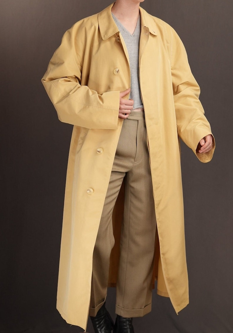 May include: A long, yellow raincoat with a button fastening and a single vent at the back. The raincoat has a classic, tailored fit and is made from a lightweight, water-resistant fabric.