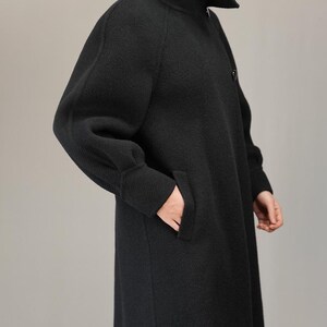 May include: A black long-sleeved coat with a high collar and a single button closure. The coat has a relaxed fit and a slightly flared silhouette.