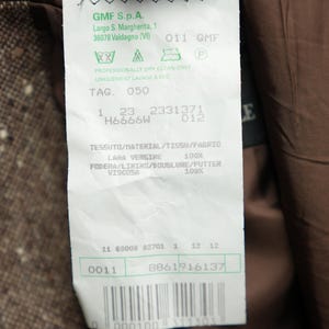 May include: A white tag with green text and symbols. The tag has the text "GMF S.p.A. Largo S. Margherita, 1 36078 Valdagno (VI) 011 GMF" and "PROFESSIONALLY DRY CLEAN ONLY UNIQUEMENT LAVAGE A SEC TAG. 050 1 23 2331371 H6666W 012 E TESSUTO/HATERIAL/TISSU/FABRIC LAHA VERGINE 100% FODERA/LINING/DOUBLURE/FUTTER VISCOSA 100% 11 88008 82701 1 12 12 0011 8861916137 0 000100 311303".