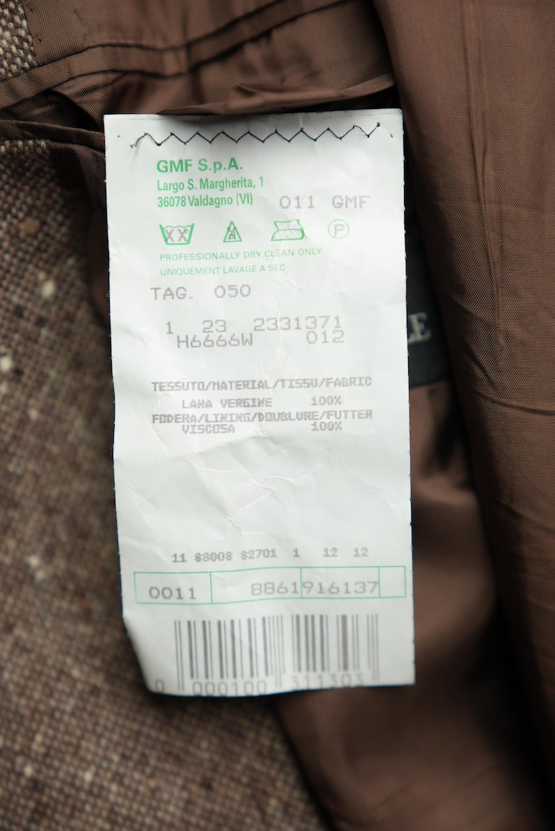 May include: A white tag with green text and symbols. The tag has the text "GMF S.p.A. Largo S. Margherita, 1 36078 Valdagno (VI) 011 GMF" and "PROFESSIONALLY DRY CLEAN ONLY UNIQUEMENT LAVAGE A SEC TAG. 050 1 23 2331371 H6666W 012 E TESSUTO/HATERIAL/TISSU/FABRIC LAHA VERGINE 100% FODERA/LINING/DOUBLURE/FUTTER VISCOSA 100% 11 88008 82701 1 12 12 0011 8861916137 0 000100 311303".