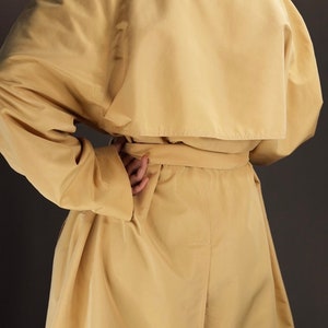 May include: A long, light yellow trench coat with a belt. The coat has a classic design with a collar and lapels.
