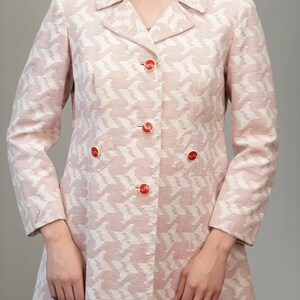 Puede incluir: Una chaqueta de color rosa y blanco con estampado, cierre de botones y mangas largas. La chaqueta tiene botones rojos y un dobladillo ligeramente acampanado.