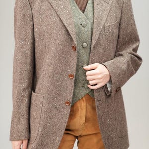 May include: A brown tweed blazer with a green waistcoat underneath. The blazer has a single-breasted closure with four buttons and flap pockets.