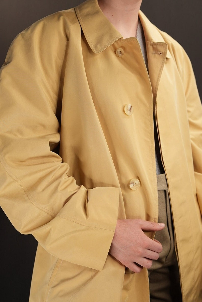 May include: A yellow raincoat with a button fastening and a single pocket on the left side.