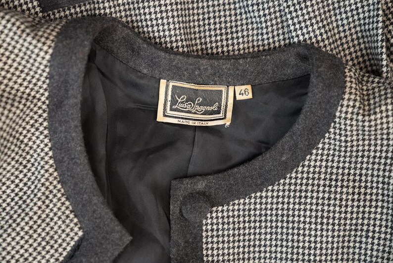 May include: A black and white houndstooth jacket with a black collar and a label that reads "Luis Lagnol" and "Made in Italy". The label also has a size tag that reads "46".