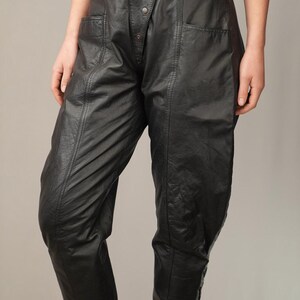 May include: Black leather pants with a high waist and a button fly. The pants have a unique design with a diagonal seam and a flap pocket on each side.