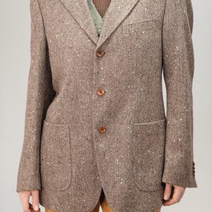 May include: A brown tweed blazer with three buttons and two pockets. The blazer has a speckled pattern.