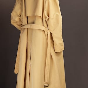 May include: A long, yellow trench coat with a belt and a single button fastening. The coat has a relaxed fit and a slightly oversized silhouette.