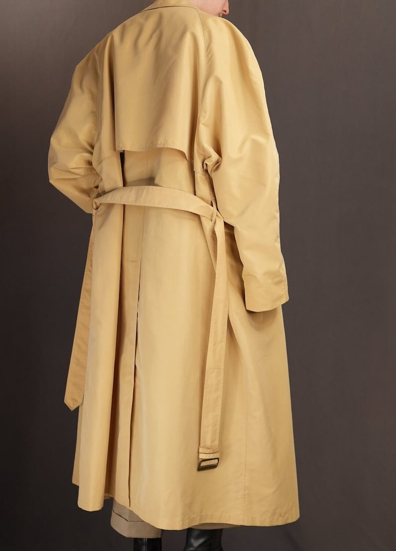 May include: A long, yellow trench coat with a belt and a single button fastening. The coat has a relaxed fit and a slightly oversized silhouette.