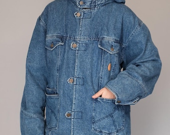 May include: A blue denim jacket featuring a hood, long sleeves, and a front button closure with toggle-style tabs. The jacket includes two chest pockets with flaps and two large lower patch pockets, finished with a brown circular patch detail.