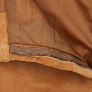 May include: Close-up of a brown suede jacket with a zipper closure. The zipper is visible and the jacket is folded back to show the lining.