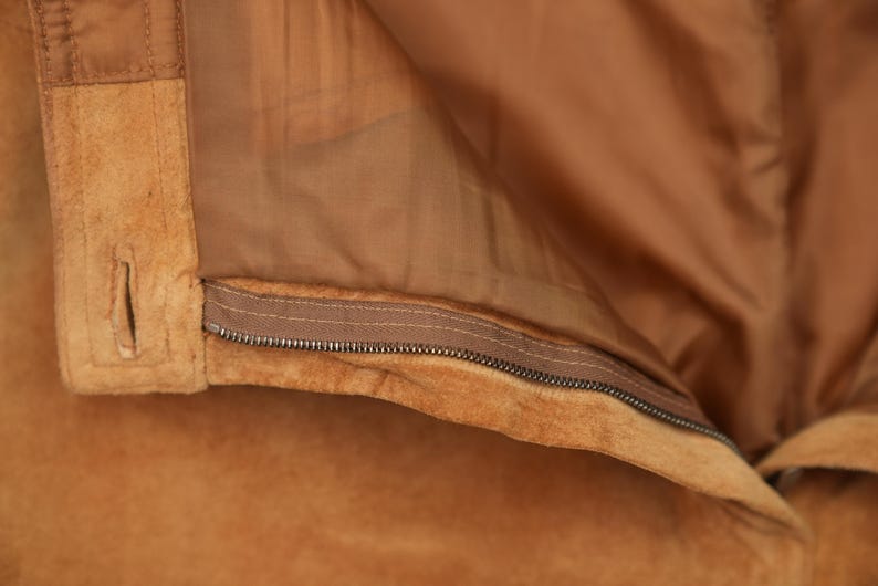 May include: Close-up of a brown suede jacket with a zipper closure. The zipper is visible and the jacket is folded back to show the lining.