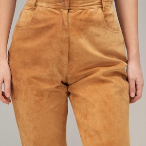 May include: A pair of high-waisted brown suede pants with a button and zipper closure. The pants have a relaxed fit and are made of a soft, supple suede.