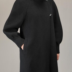 May include: A black long-sleeved coat with a high collar and a button closure. The coat has a slightly flared silhouette and a textured fabric.