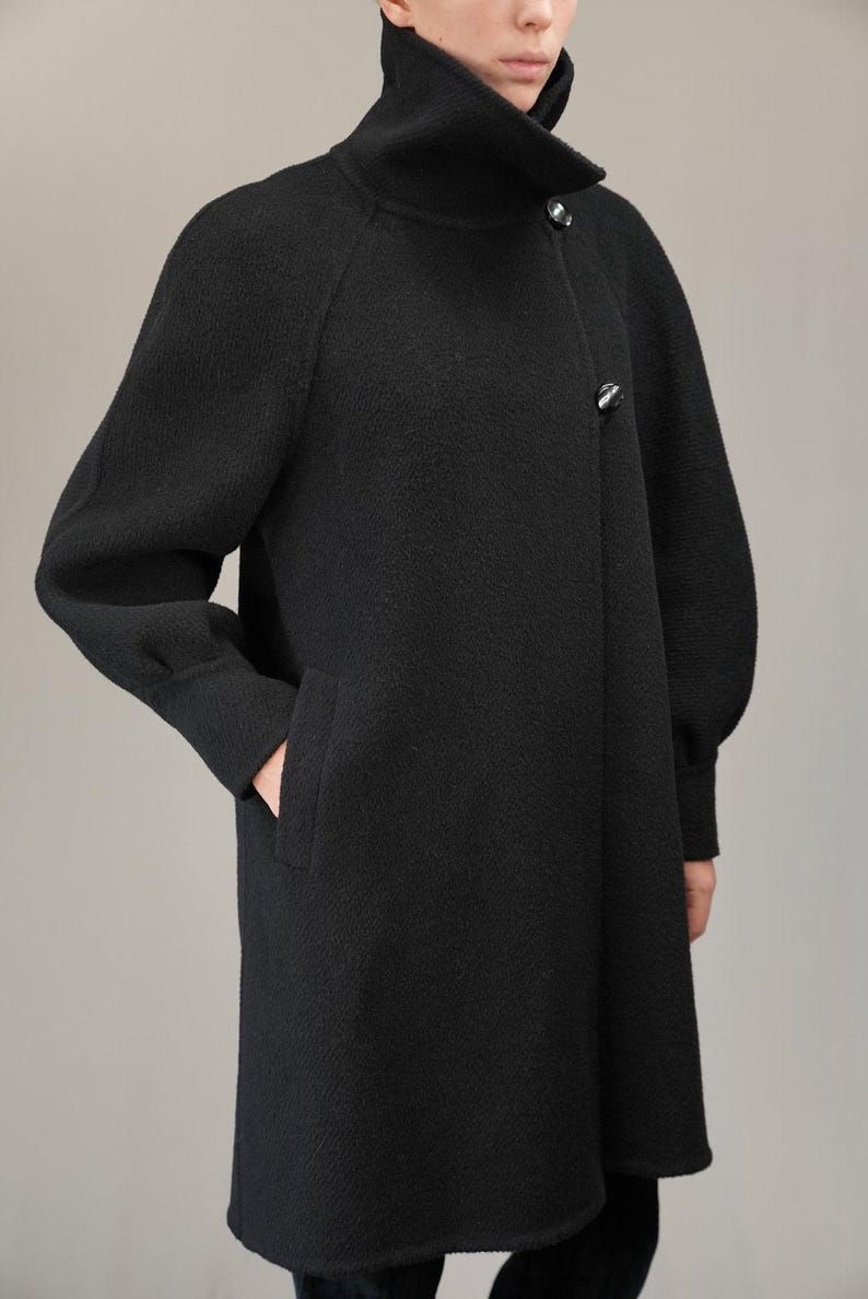 May include: A black long-sleeved coat with a high collar and a button closure. The coat has a slightly flared silhouette and a textured fabric.