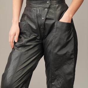 May include: Black leather pants with a high waist and a button fly. The pants have a slim fit and are made of a soft, supple leather.