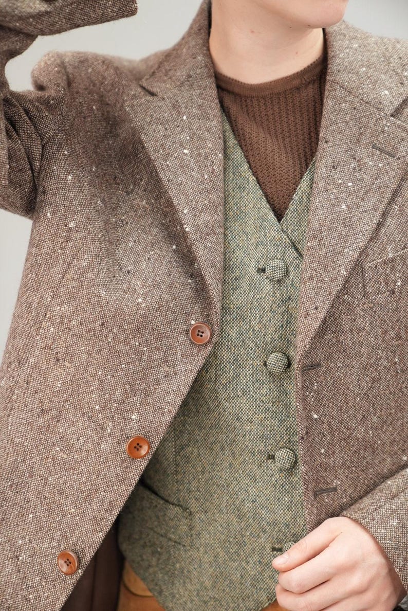 May include: A brown tweed jacket with a matching brown tweed waistcoat. The jacket has a button fastening and the waistcoat has a button fastening and a pocket on the left side.