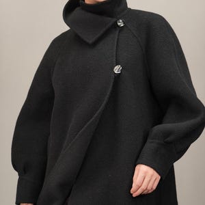 May include: A black long-sleeved coat with a high collar and a single button closure. The coat has a relaxed fit and a slightly oversized silhouette.