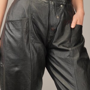 May include: Black leather pants with a high waist and a button fly. The pants have a relaxed fit and a slightly flared leg.