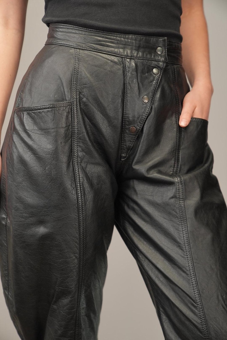 May include: Black leather pants with a high waist and a button fly. The pants have a relaxed fit and a slightly flared leg.