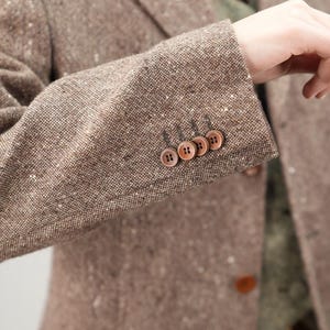 May include: A brown tweed blazer with a speckled pattern and four brown buttons on the cuff.