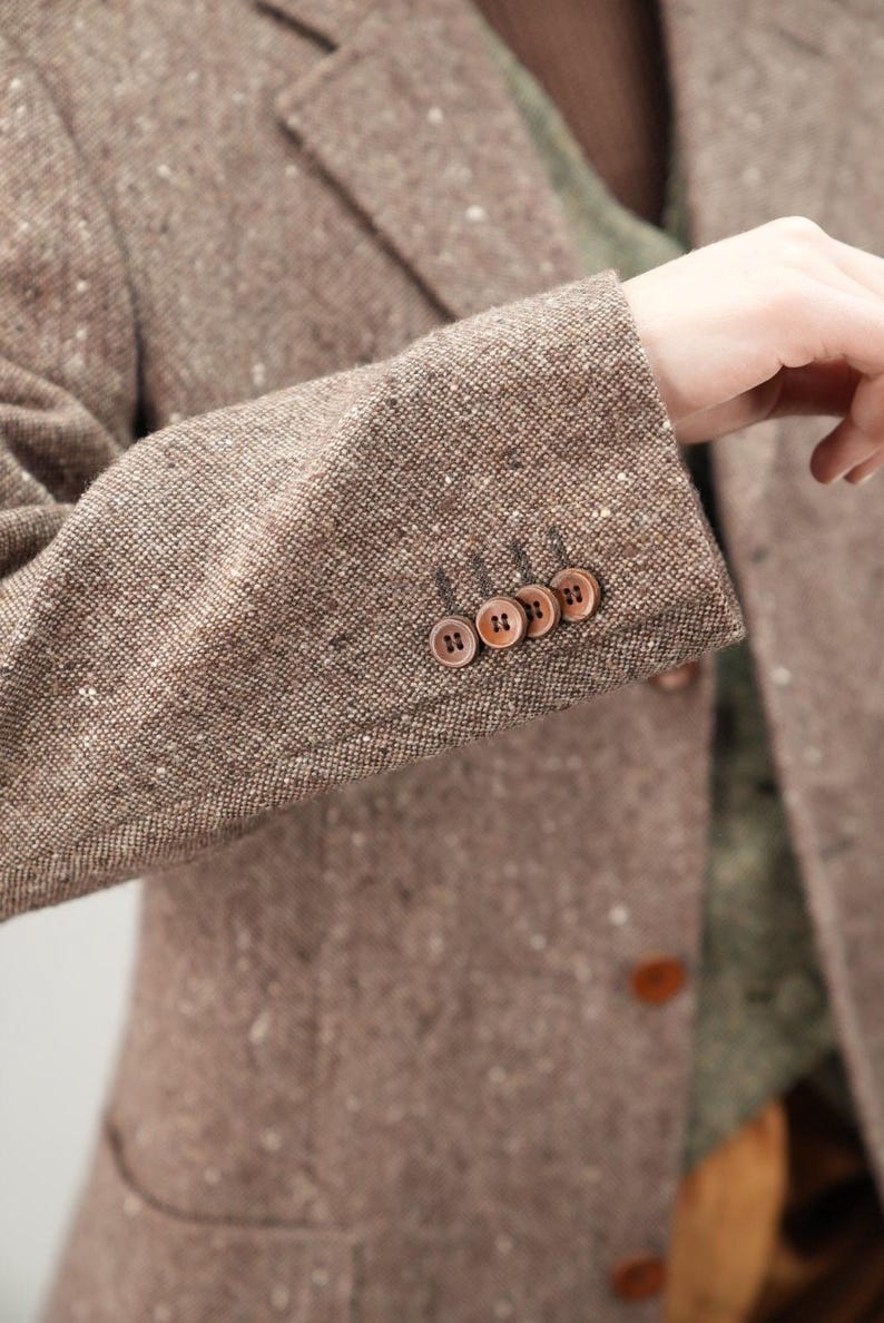 May include: A brown tweed blazer with a speckled pattern and four brown buttons on the cuff.