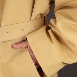 May include: A beige trench coat with a belt and a pocket. The coat is made of a smooth, lightweight fabric.