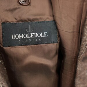 May include: A brown tweed jacket with a black label that reads "UOMO LEBOLE CLASSIC" in white lettering.