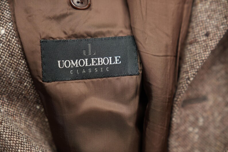 May include: A brown tweed jacket with a black label that reads "UOMO LEBOLE CLASSIC" in white lettering.