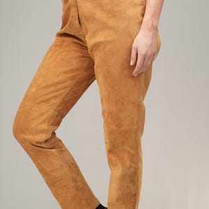 May include: A pair of high-waisted, light brown suede pants. The pants have a straight leg and a relaxed fit.