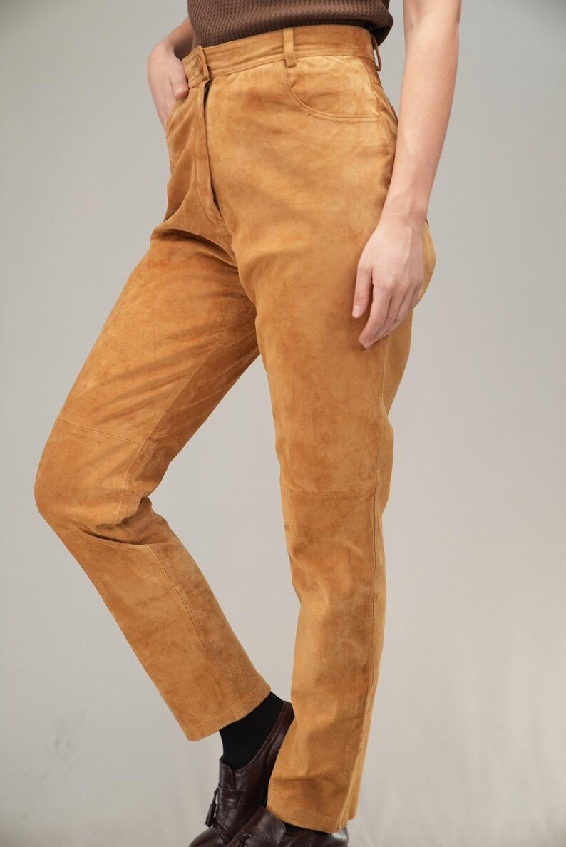 May include: A pair of high-waisted, light brown suede pants. The pants have a straight leg and a relaxed fit.