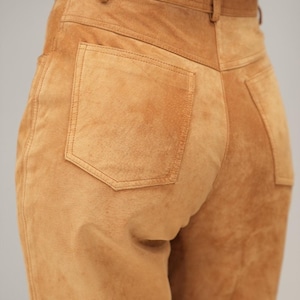 May include: A pair of brown suede pants with a back pocket. The pants have a high waist and a straight leg.