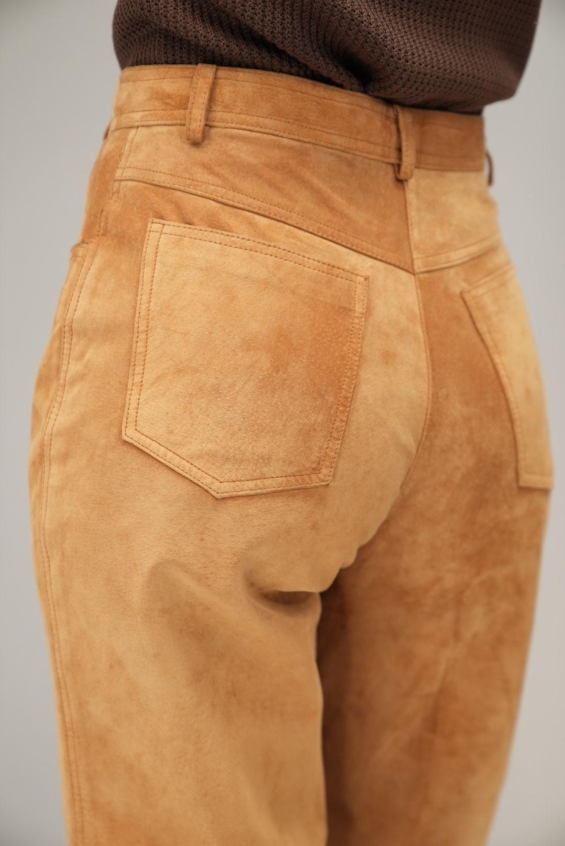 May include: A pair of brown suede pants with a back pocket. The pants have a high waist and a straight leg.