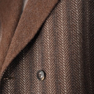 K&ouml;nnte beinhalten: Nahaufnahme einer braunen Jacke aus Tweed mit Fischgr&auml;tenmuster, braunem Kragen und einem einzigen Knopf.