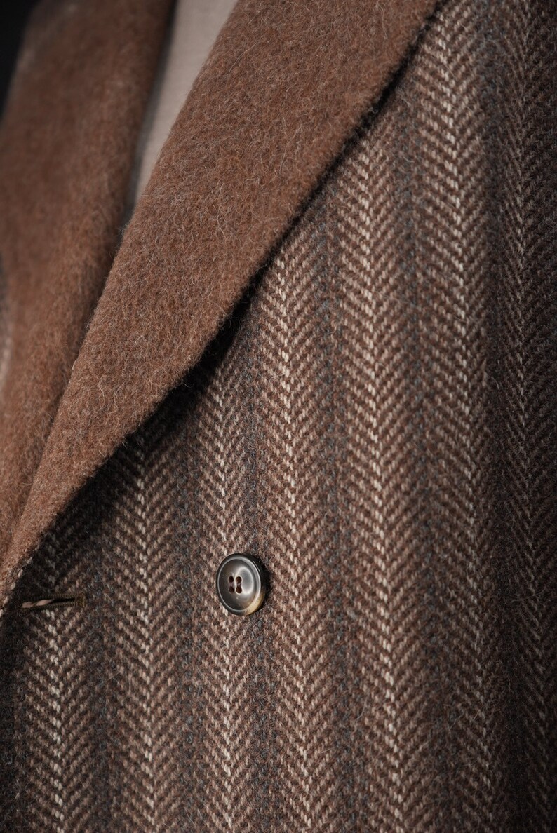 K&ouml;nnte beinhalten: Nahaufnahme einer braunen Jacke aus Tweed mit Fischgr&auml;tenmuster, braunem Kragen und einem einzigen Knopf.