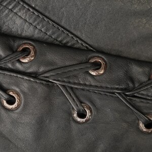 May include: Close-up of black leather with a series of decorative metal eyelets and lacing.