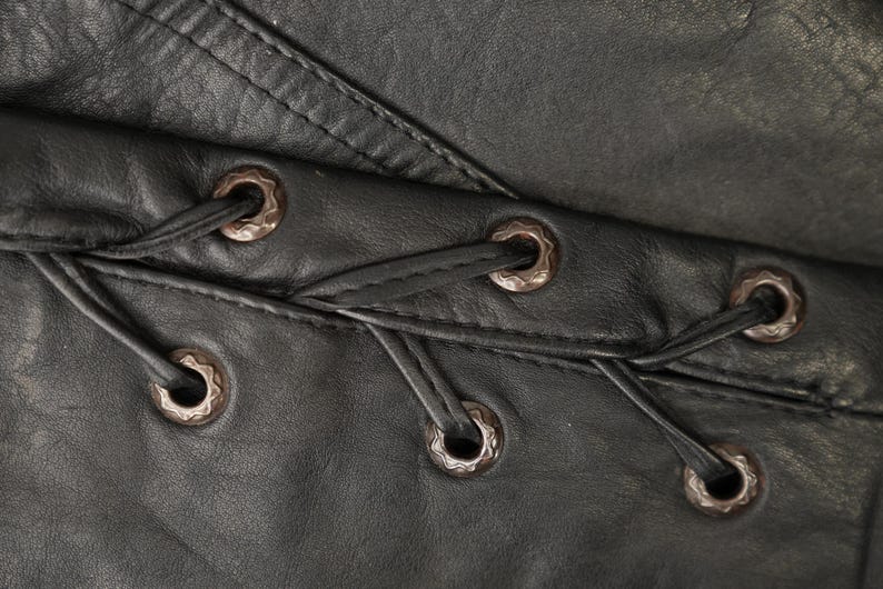 May include: Close-up of black leather with a series of decorative metal eyelets and lacing.