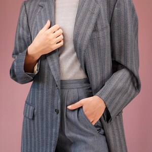 Puede incluir: Una chaqueta azul a rayas con un cierre de un botón. La chaqueta está hecha de una tela texturizada y tiene un corte holgado.