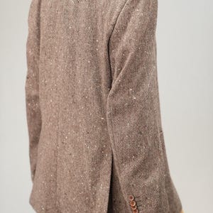 May include: A brown tweed blazer with a speckled pattern. The blazer has a single button closure and a flap pocket on the left side.