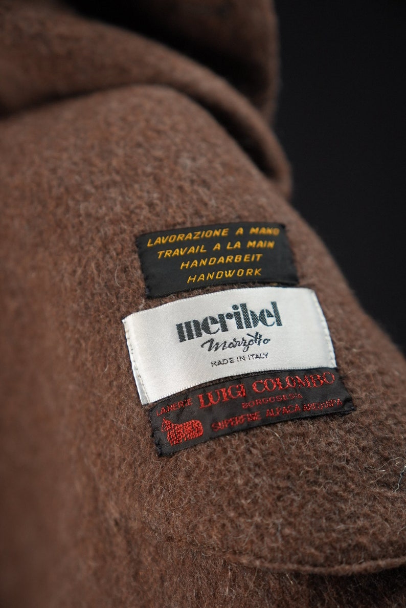 K&ouml;nnte beinhalten: Nahaufnahme eines braunen Wollstoffes mit einem wei&szlig;en Etikett, auf dem "meribel Marretto Made in Italy" steht, und einem braunen Etikett, auf dem "L.ANERIE LUIGI COLOMBO BORGOSESA SUPREME ALPACA MERINO" steht. Das Etikett enth&auml;lt auch den Text "LAVORAZIONE A MANO TRAVAIL A LA MAIN HANDARBEIT HANDWORK".