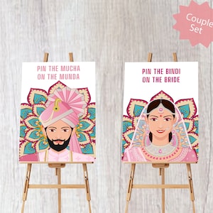 May include: Two white game boards with colorful illustrations of a bride and groom in traditional Indian wedding attire. The text on the boards reads "Pin the Mucha on the Munda" and "Pin the Bindi on the Bride".