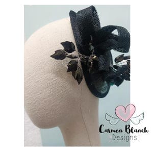 May include: Black and silver hair comb with a black net and a bow. The comb is decorated with black leaves and rhinestones. The comb is on a white mannequin head. The text "Carmen Blanch Designs" is visible in the bottom right corner of the image.