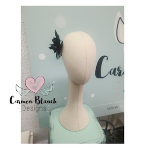 May include: A black feather hair clip with a delicate design. The clip is displayed on a white mannequin head.