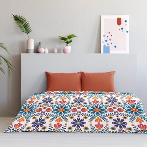 May include: A white duvet cover with a colorful floral pattern featuring blue, orange, yellow, red, and purple flowers. The duvet cover is on a bed with two orange pillows.