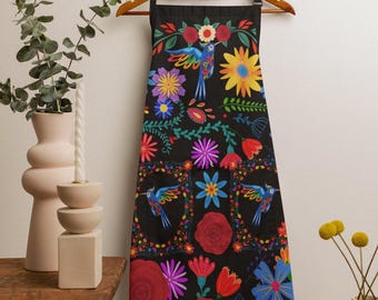 May include: Black apron with a vibrant floral and hummingbird design. The apron features colorful flowers, including red roses, yellow sunflowers, and blue and purple blooms. The design includes hummingbirds and decorative borders.