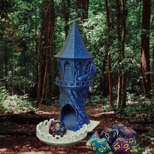 Könnte beinhalten: Ein blauer und weißer 3D-gedruckter Turm mit einer Wendeltreppe und einem Würfeltablett. Der Turm steht auf einem Waldboden mit grünen Blättern und brauner Erde. Das Würfeltablett hat eine weiße Basis und ein blaues und weißes Turmdessin. Es befinden sich mehrere blaue und weiße Würfel mit gelben Zahlen im Tablett.